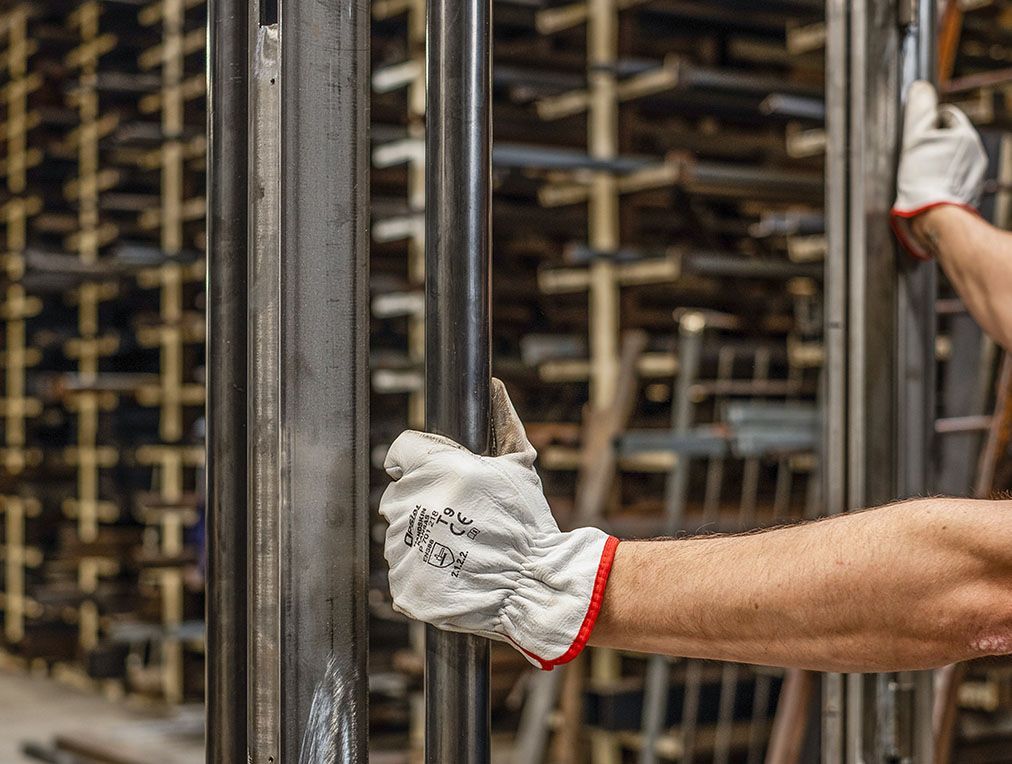 Personne portant des gants manipulant des barres métalliques dans un entrepôt.