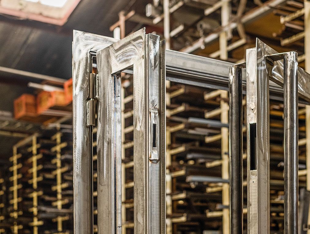 Cadres de portes métalliques dans une usine, avec des étagères de matériaux en arrière-plan.