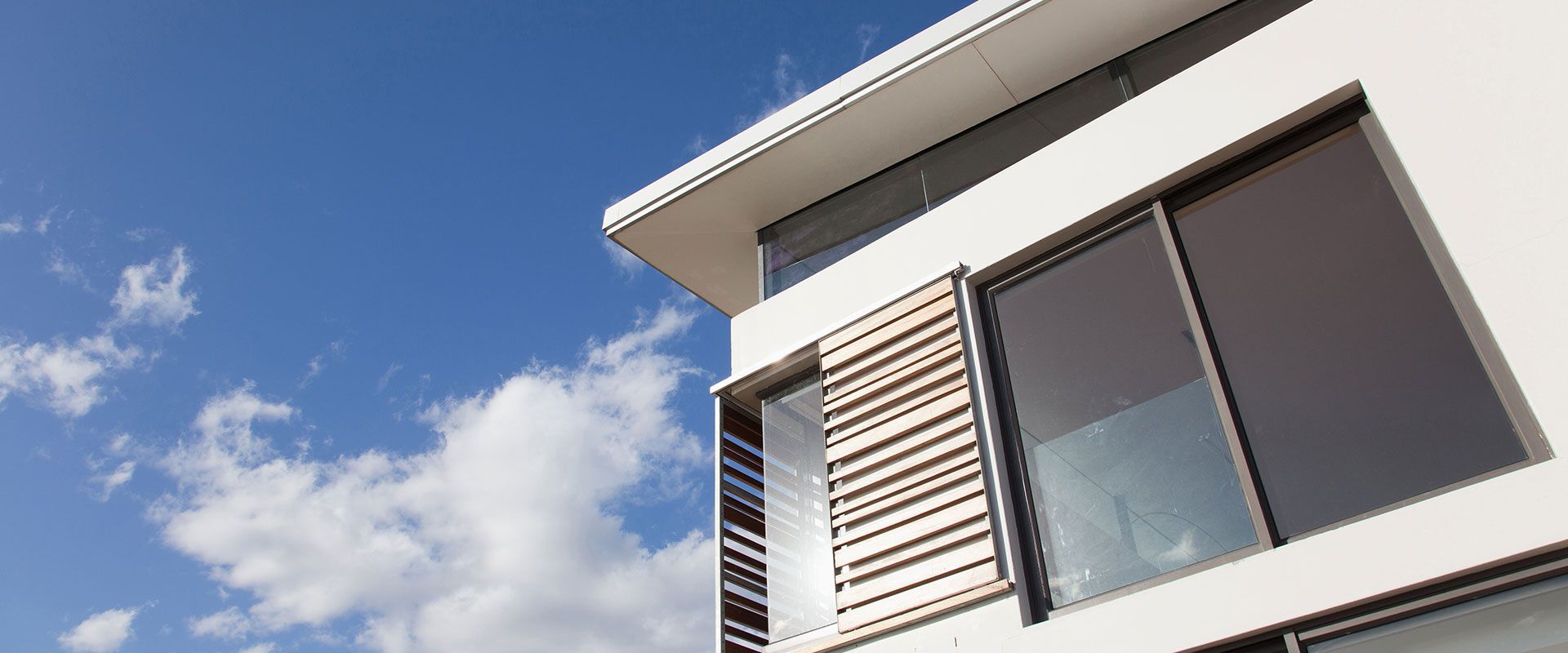 Bâtiment moderne avec de grandes fenêtres se détachant sur un ciel bleu nuageux.