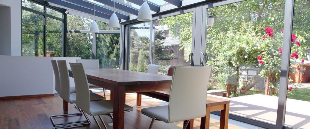 Salle à manger avec table en bois, chaises couleur crème et baies vitrées donnant sur un jardin aux fleurs roses.
