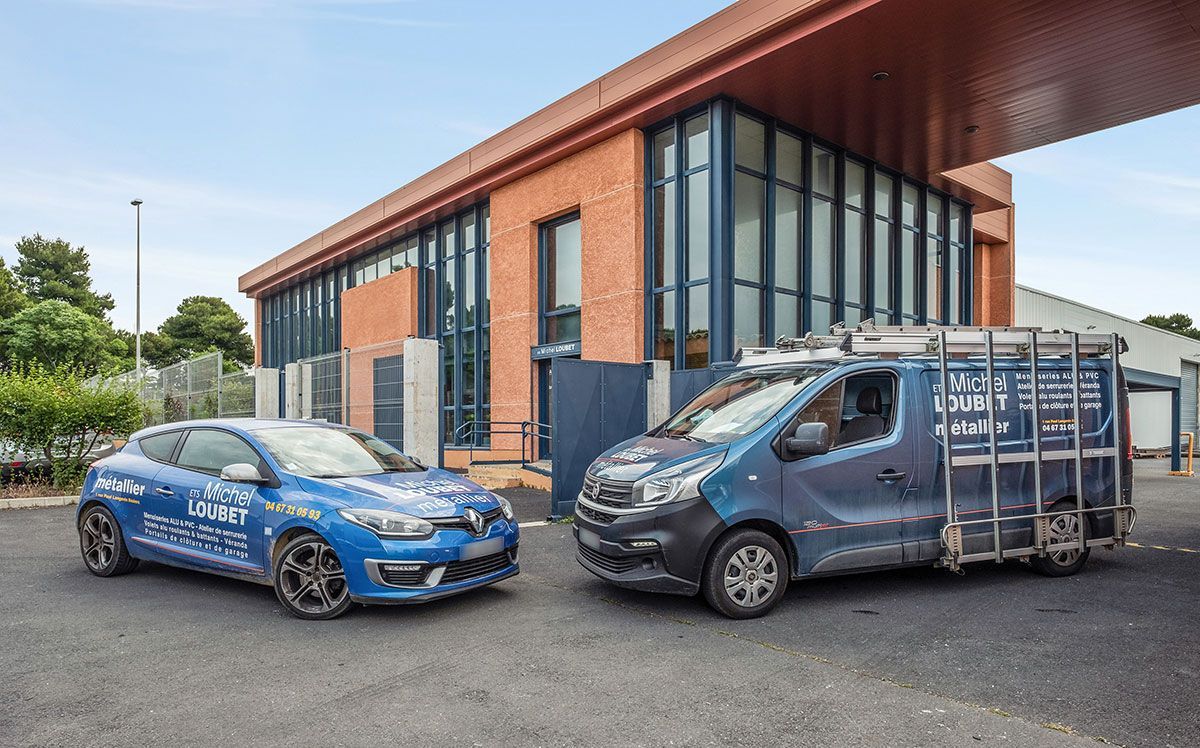 Une Renault bleue et une camionnette sont garées devant un bâtiment en briques. La camionnette est équipée d'une cage métallique à l'arrière.