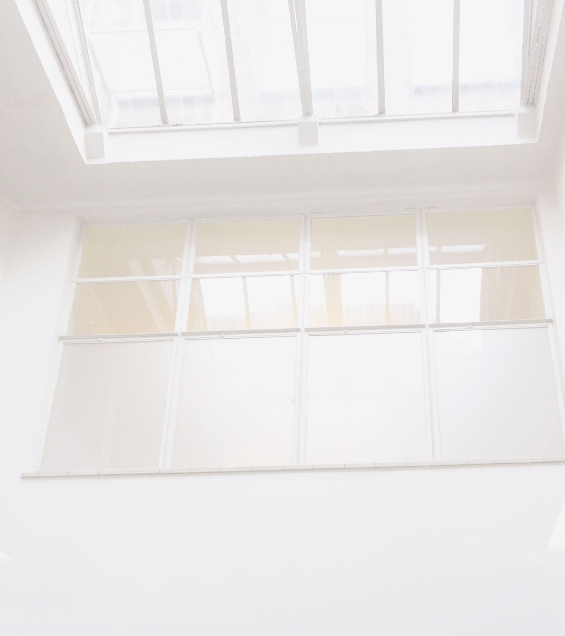 Grande fenêtre lumineuse et puits de lumière dans une pièce blanche.