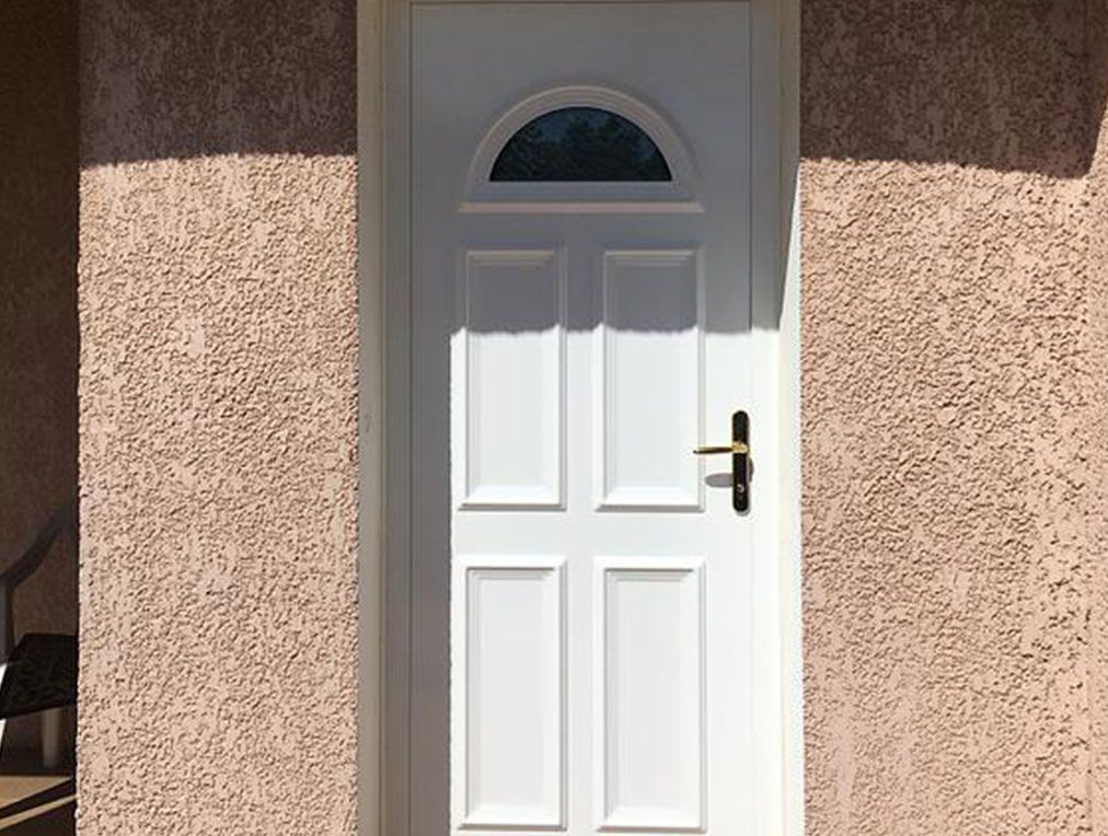 Porte blanche avec fenêtre cintrée en verre, poignée noire, encastrée dans un mur à l'aspect stuc.