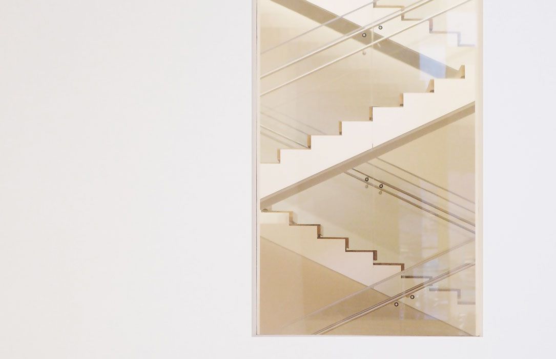 Mur blanc avec une photographie nette d'un escalier, superposée et inclinée, lumière douce.