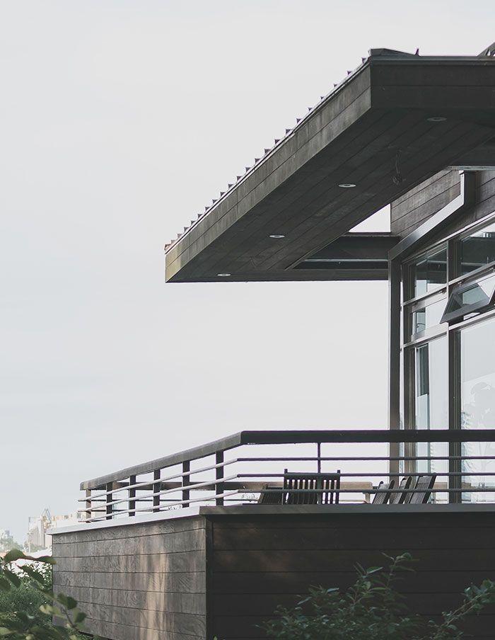Maison moderne à l'extérieur, avec un auvent en bois foncé et un balcon donnant sur une vue brumeuse.