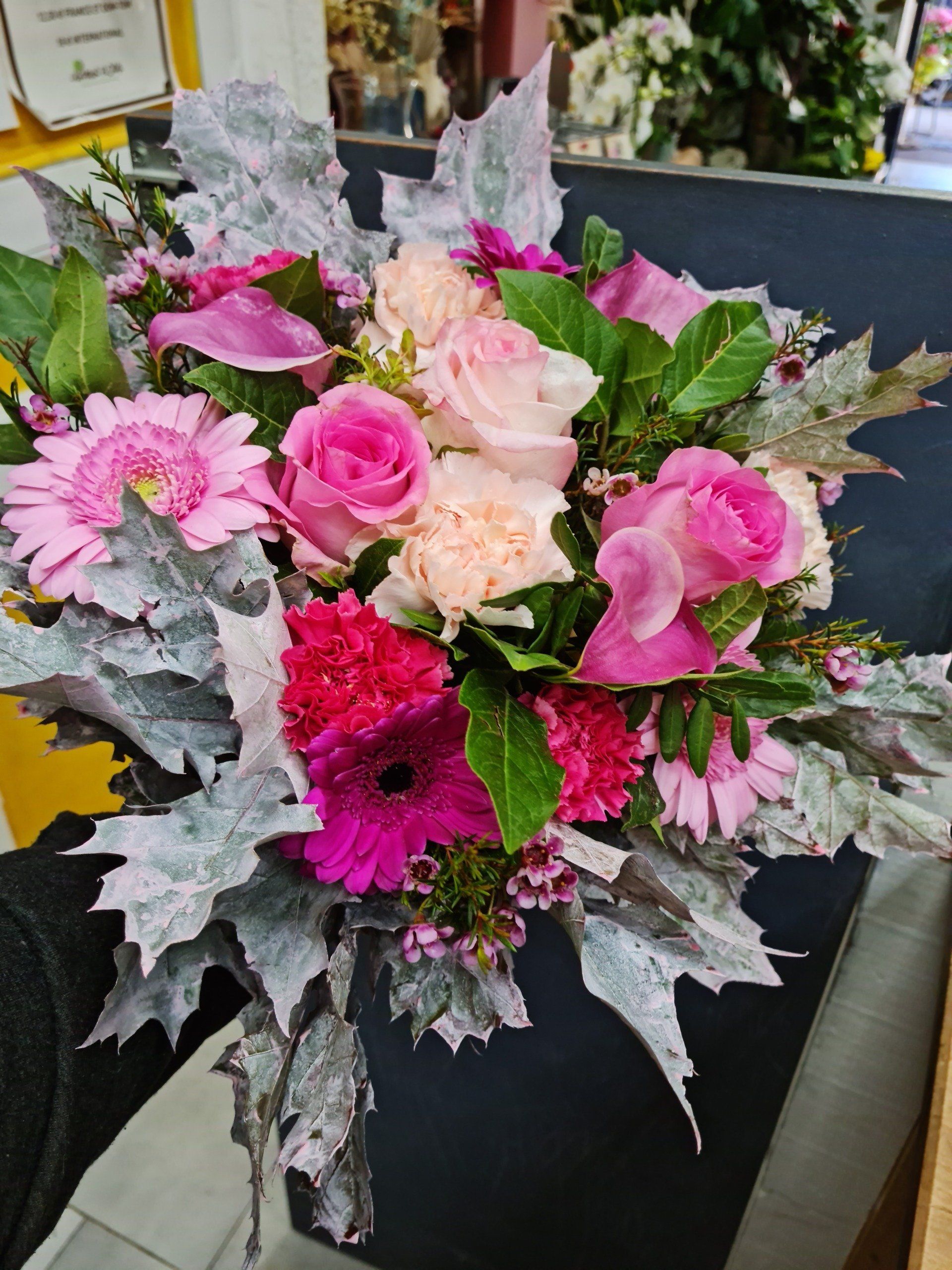 Bouquet de fleurs roses et pêche avec des gerberas, des roses et du feuillage argenté dans un vase