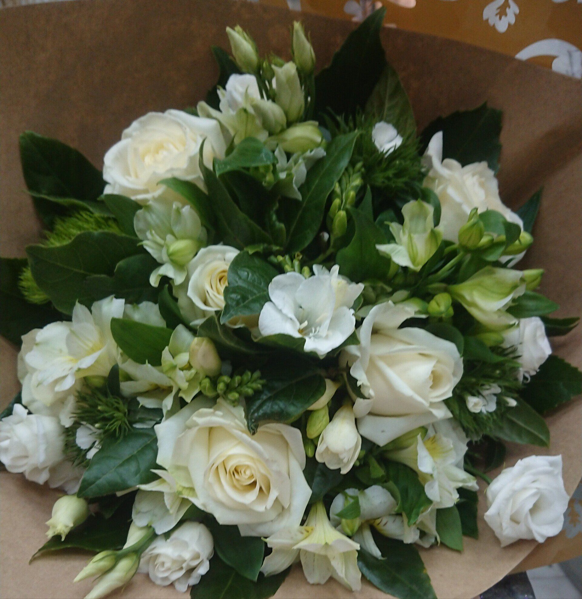 Bouquet de roses blanches et de fleurs blanches mélangées avec des feuilles vertes, emballé dans du papier kraft.