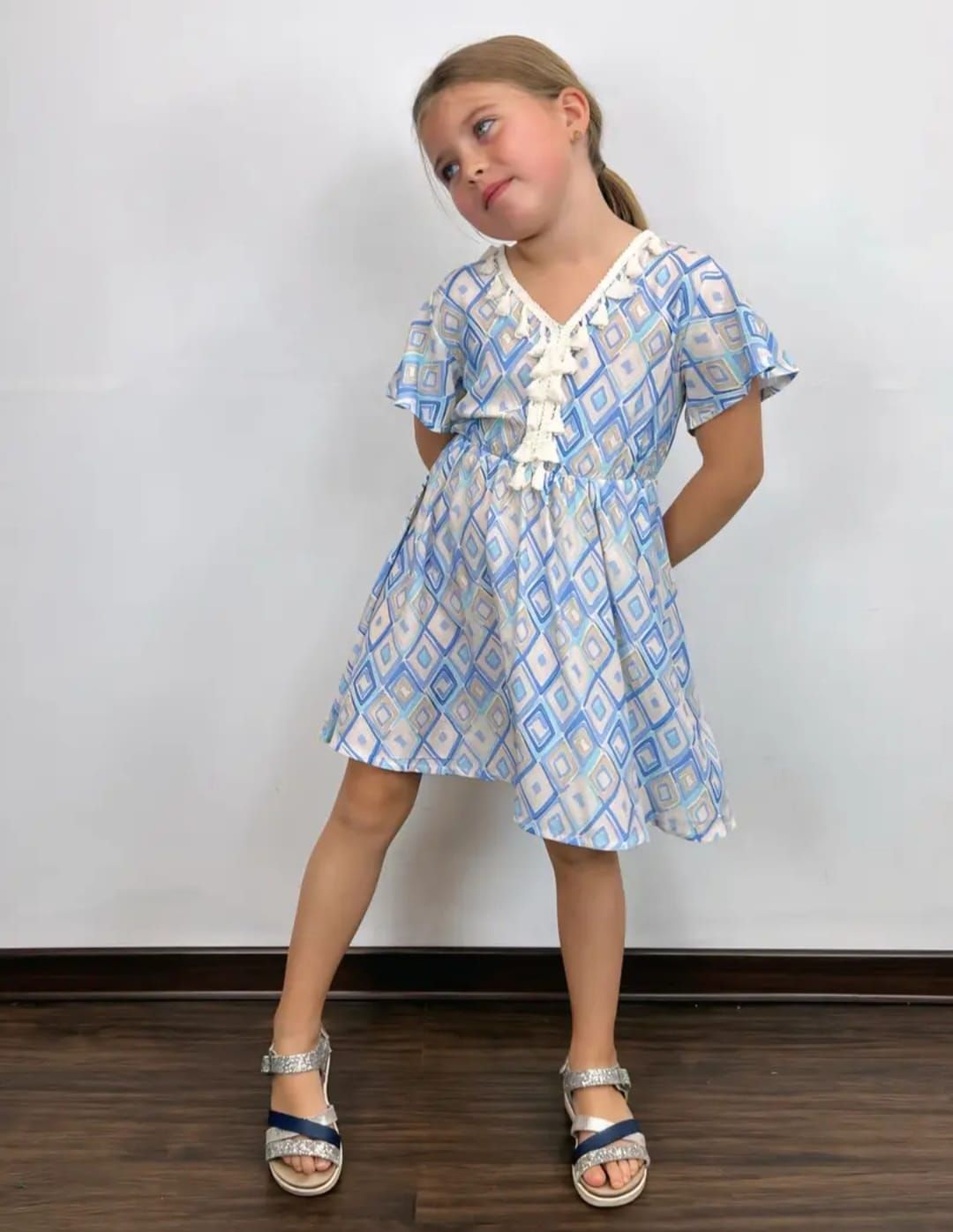 Una niña lleva un vestido azul y blanco y sandalias.