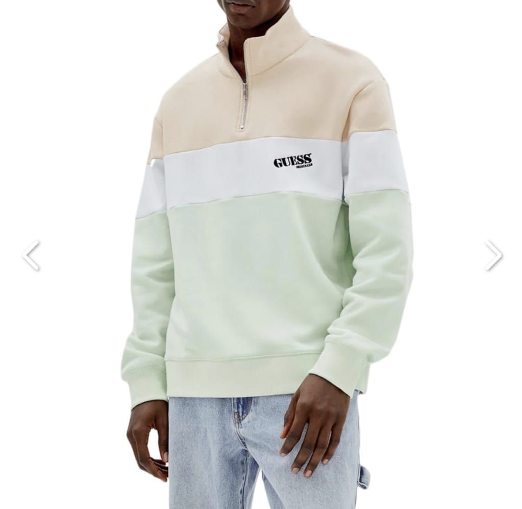 Un hombre lleva una sudadera con media cremallera y vaqueros.