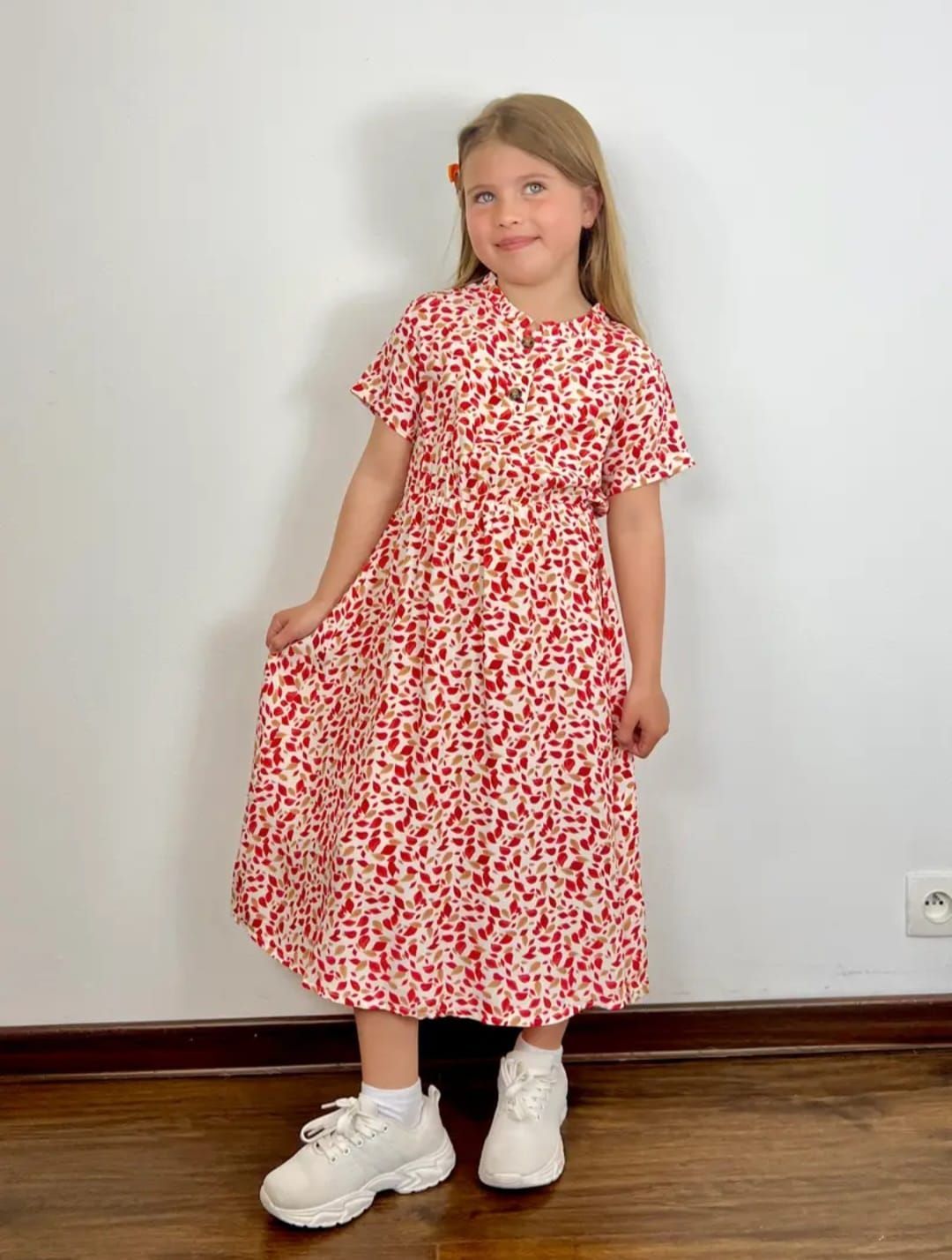 Una niña lleva un vestido rojo y blanco y zapatillas blancas.