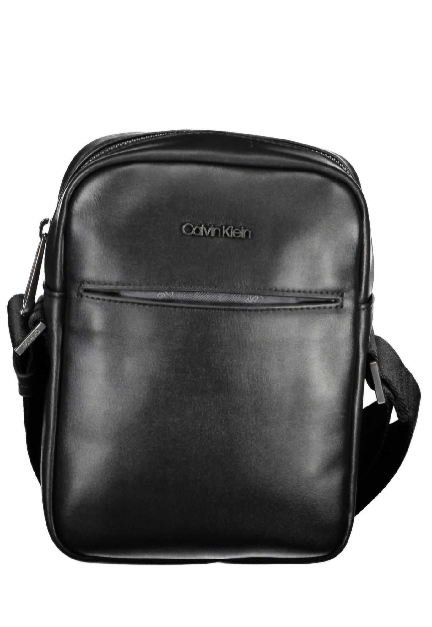 Un bolso mensajero Calvin Klein negro con una correa negra sobre un fondo blanco.