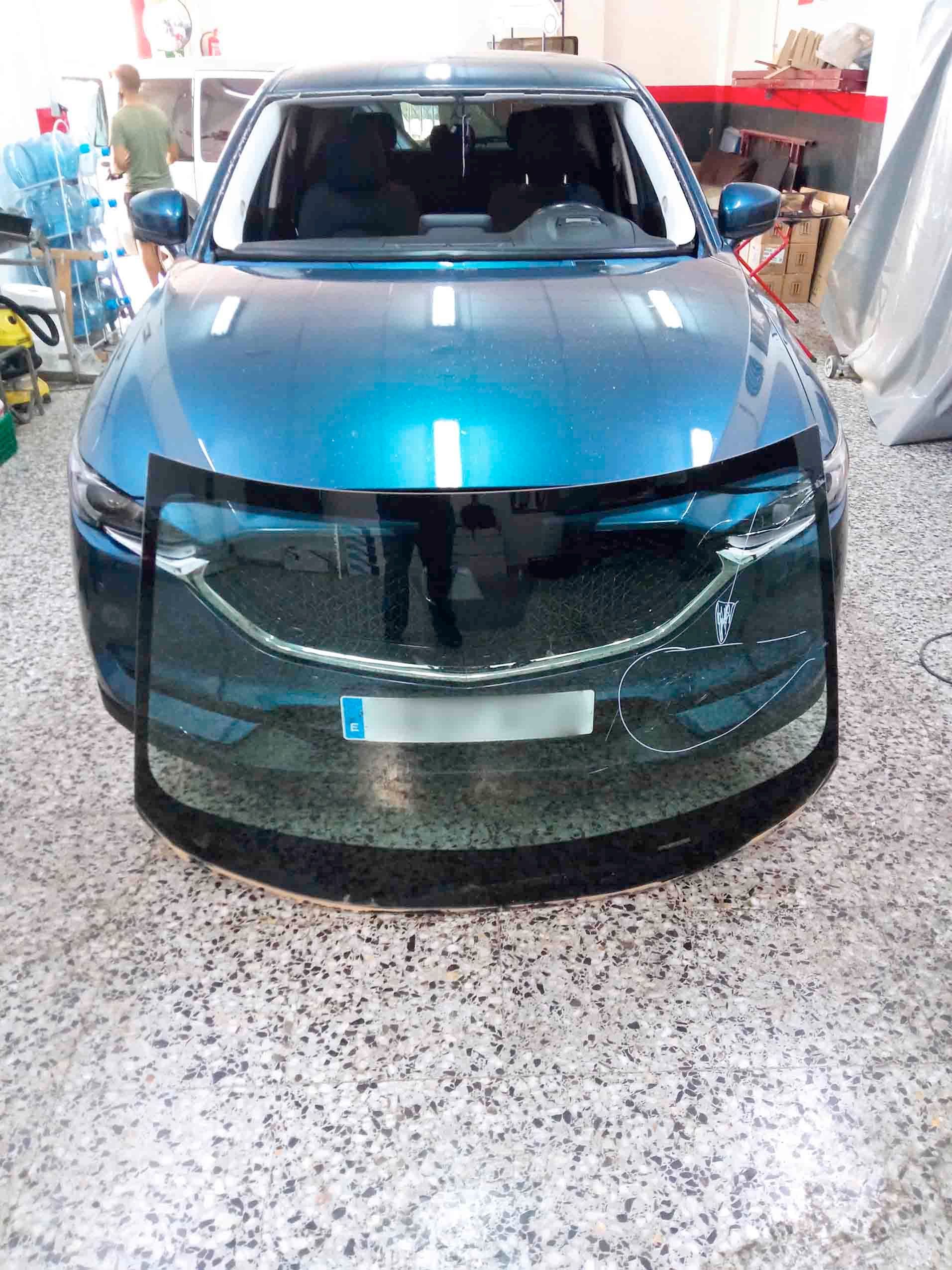 Un coche azul con el parabrisas roto está en un garaje.