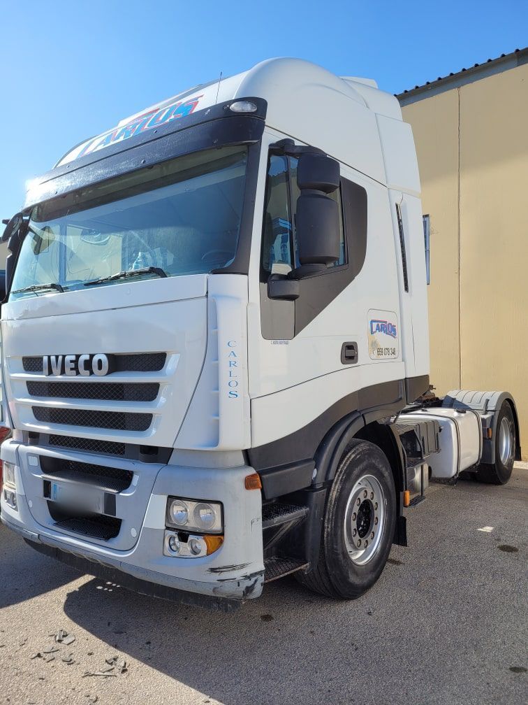 Un camión semirremolque Iveco blanco está estacionado frente a un edificio.
