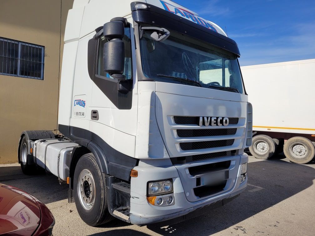 Un camión semirremolque Iveco blanco está estacionado frente a un edificio.