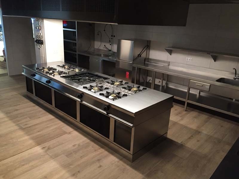 Cocina comercial moderna de acero inoxidable con horno y encimeras de preparación bajo una iluminación brillante.