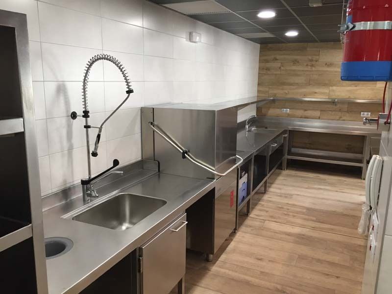 Cocina moderna con fregadero de acero inoxidable, encimera accesible, suelo de madera y estanterías abiertas.