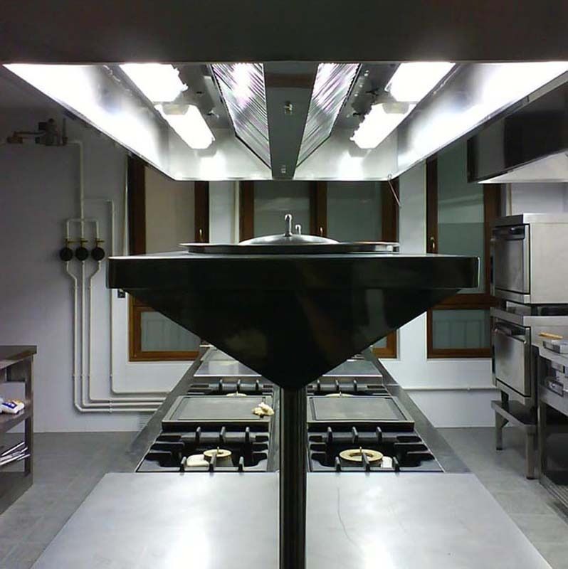 Cocina comercial moderna con equipos de acero inoxidable y campana extractora central sobre las placas de cocción.