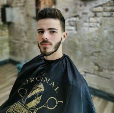 Un homme avec une barbe porte une cape dans un salon de coiffure.