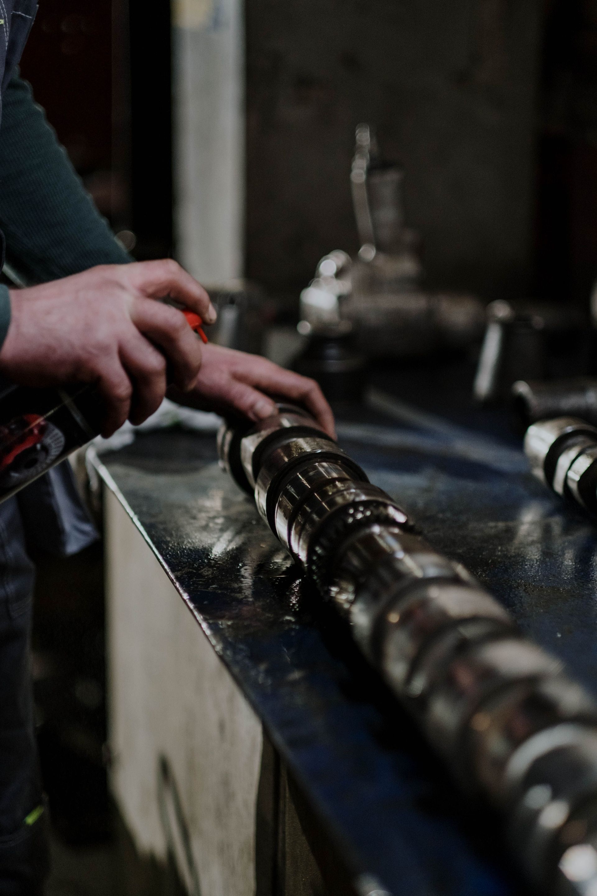 Des mains inspectent des rouleaux métalliques sur une machine dans un atelier faiblement éclairé.