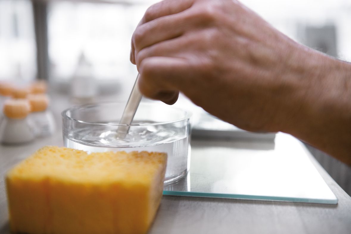 Eine Person hält einen Holzstab in einem Glas Wasser.