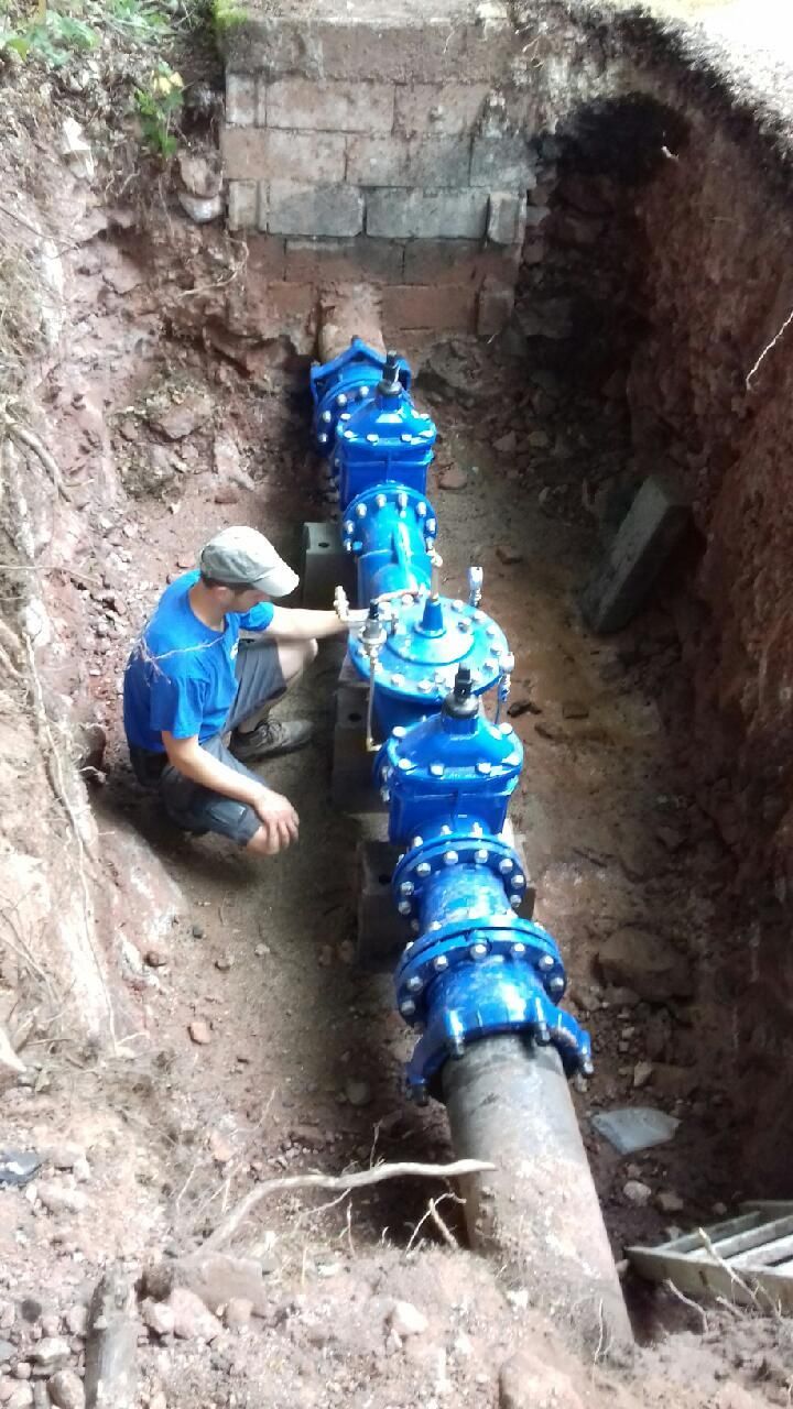 Un homme inspecte de grandes vannes d'eau bleues dans une tranchée creusée.