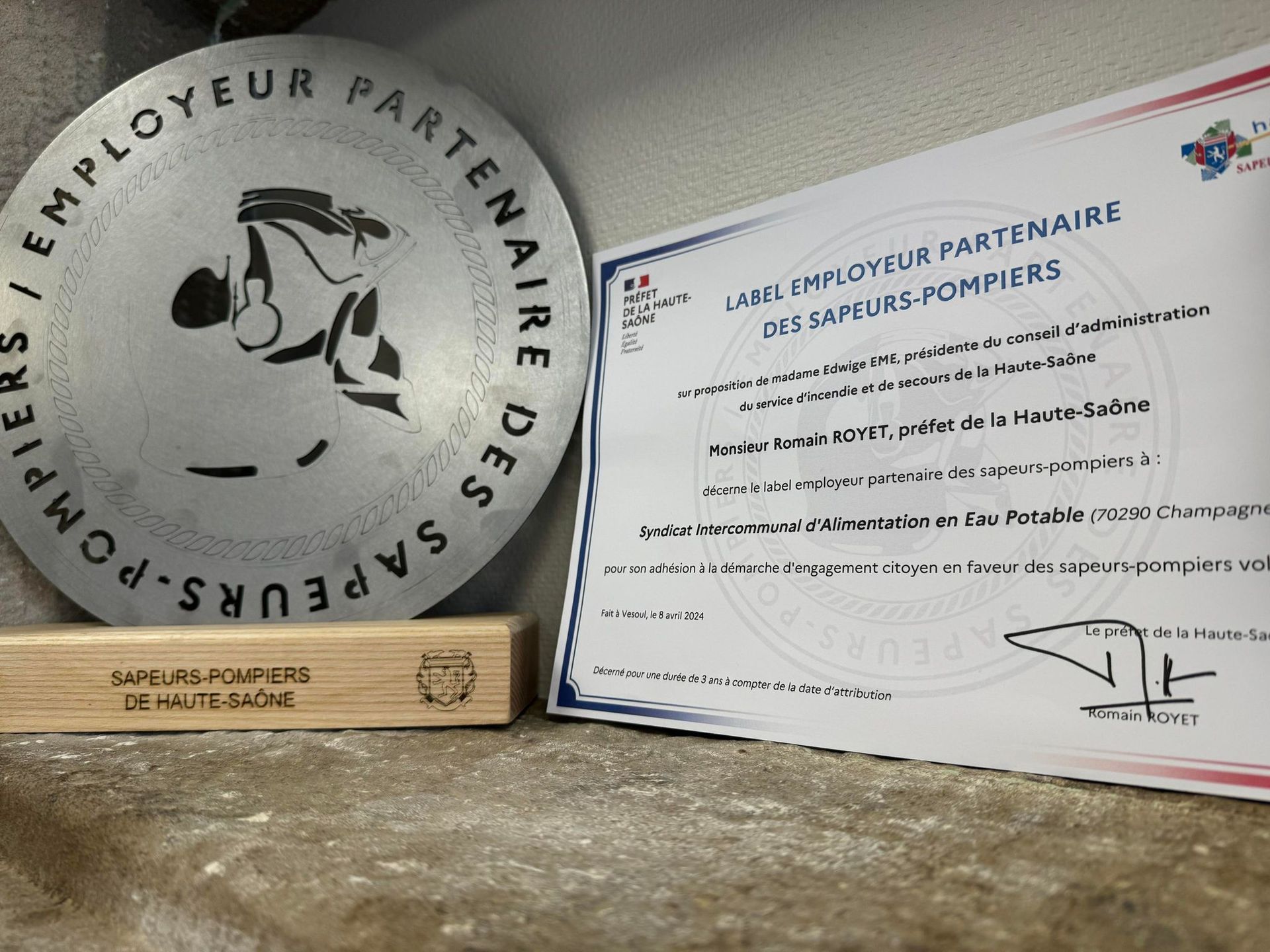 Une camionnette blanche, portant le logo « ars », est garée sur une route asphaltée mouillée, entourée de verdure.