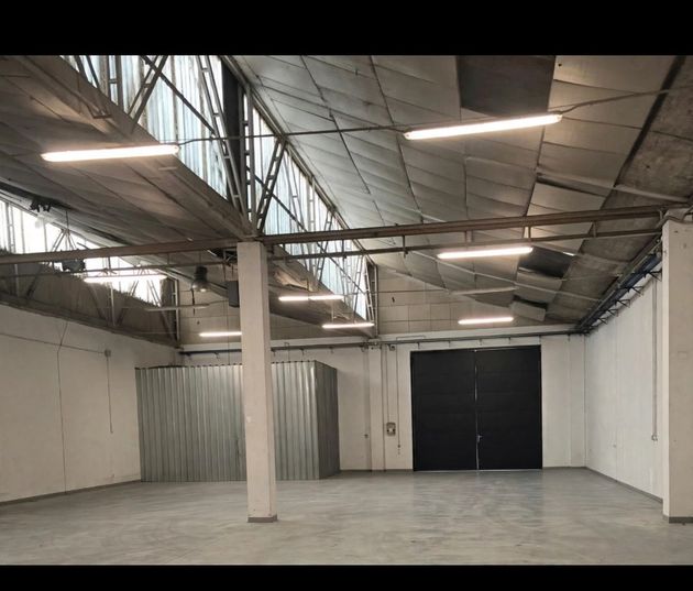 Almacén industrial vacío con paredes blancas, suelo de hormigón, techo de metal a la vista y grandes puertas dobles oscuras