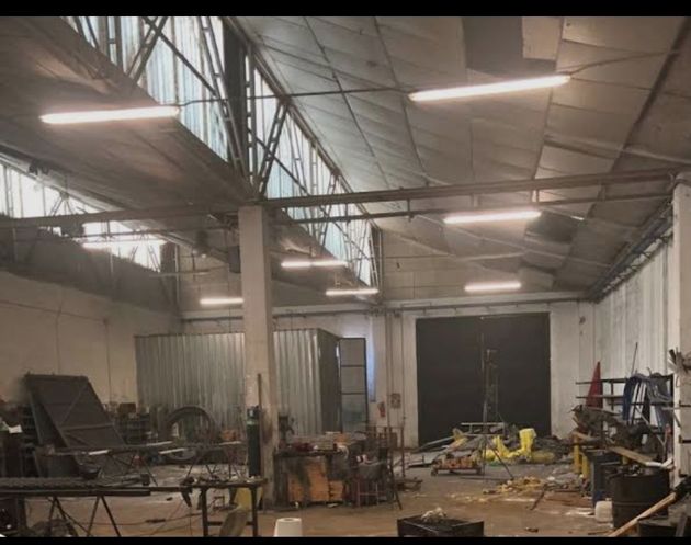 Amplio taller industrial con estructuras metálicas, herramientas y equipos bajo una iluminación intensa en el techo