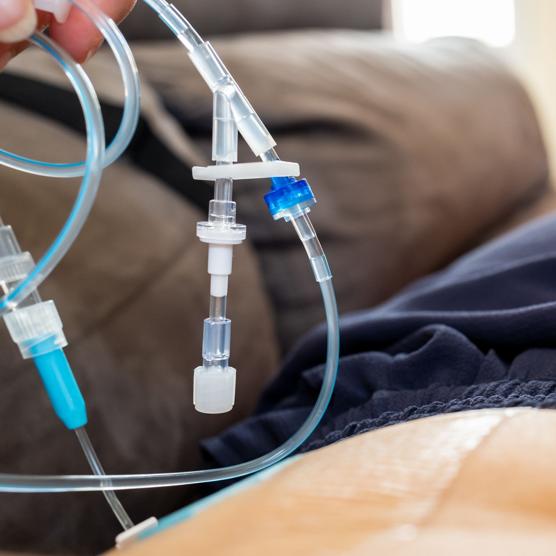 Gros plan sur une personne tenant une tubulure médicale reliée à un site de cathétérisme sur l'abdomen d'un patient.