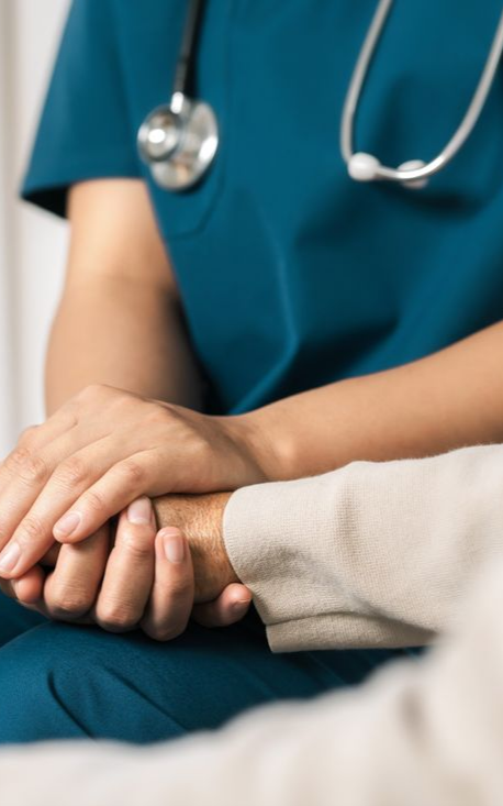 Une soignante en blouse turquoise tient la main d'un patient dans un geste de réconfort et de soutien.