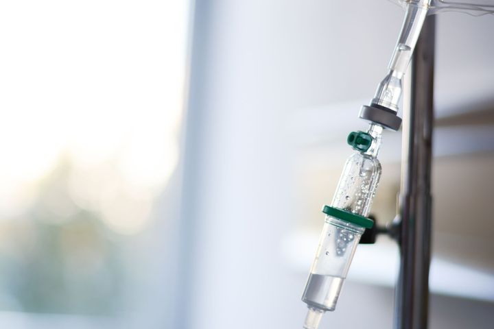 Une chambre de perfusion intraveineuse avec du liquide s'écoulant lentement dans la tubulure, sur un fond de chambre de clinique, flou et lumineux.