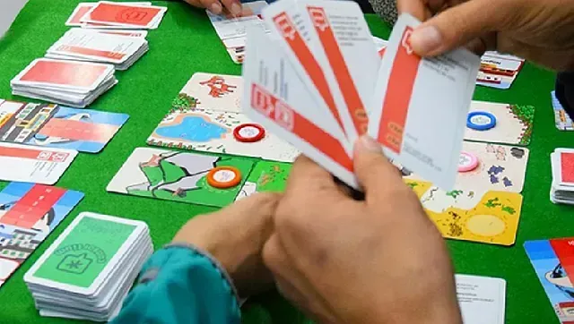 Manos con cartas rojas y blancas juegan sobre una mesa de fieltro verde. Se colocan otras cartas y fichas.