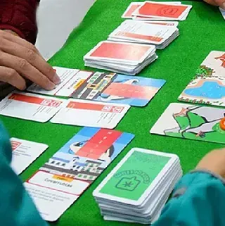 Personas jugando a las cartas sobre una superficie de fieltro verde, con cartas extendidas y sostenidas en la mano.