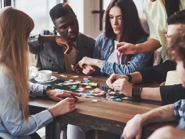Grupo de amigos diversos jugando a un juego de mesa en una mesa de madera en una cafetería. Expresiones concentradas, fichas coloridas.