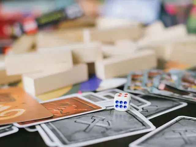 Dados que muestran un seis sobre una pila de cartas de juego, con bloques de madera y más cartas en el fondo.