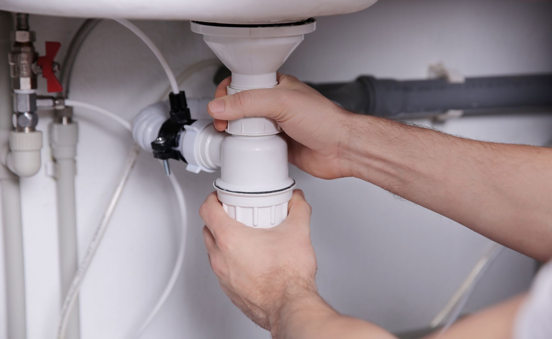 Des mains installent un tuyau d'évacuation d'évier en PVC blanc sous un lavabo de salle de bains.