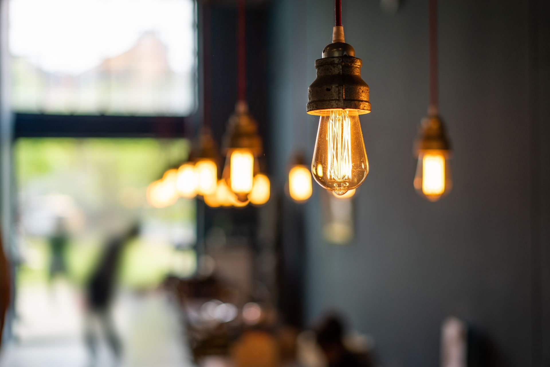 Des ampoules Edison suspendues, à la lumière chaude, éclairent l'intérieur tamisé d'un café, avec une fenêtre floue en arrière-plan.
