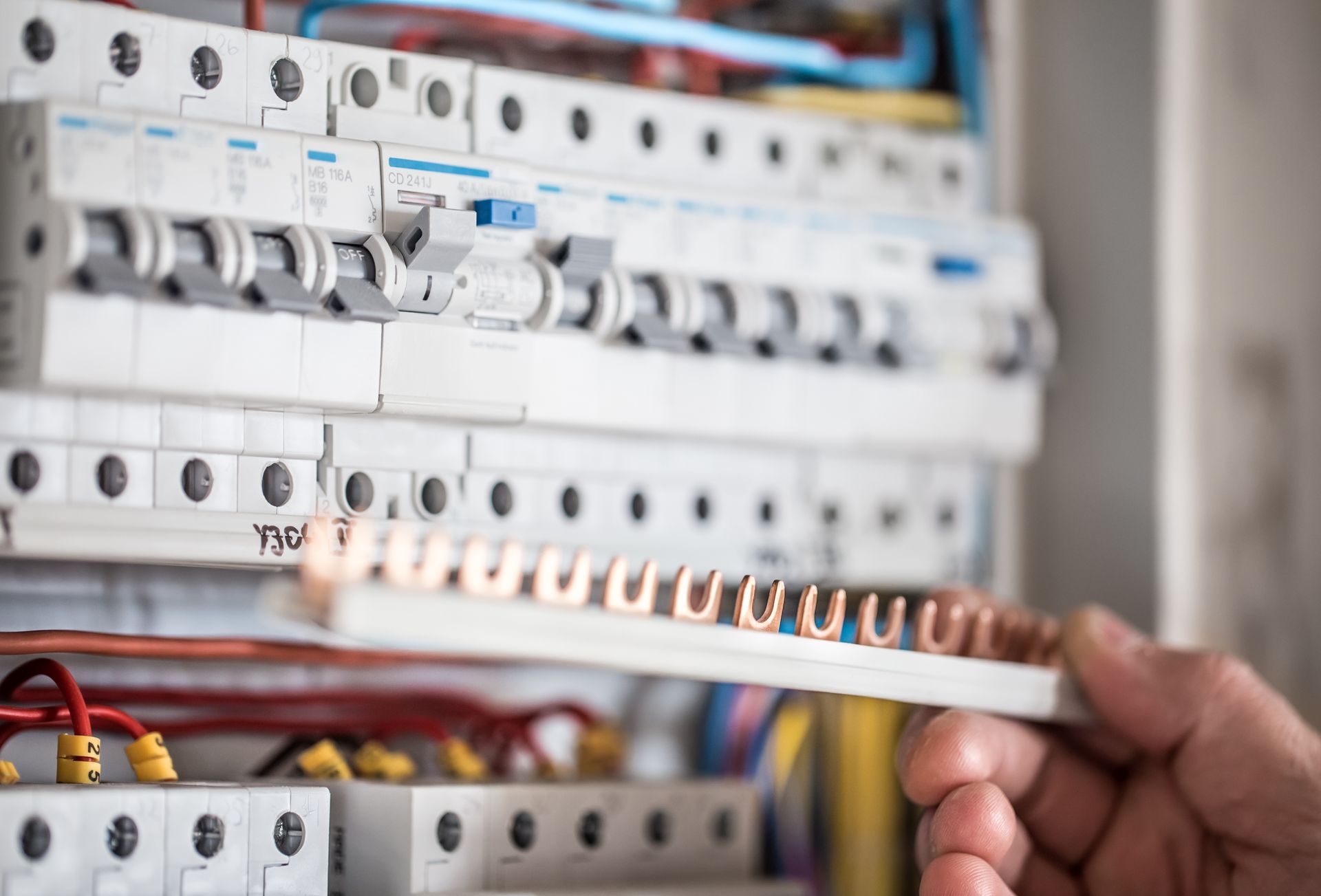 Main tenant un dénudeur de fil près d'un tableau électrique comportant des rangées d'interrupteurs