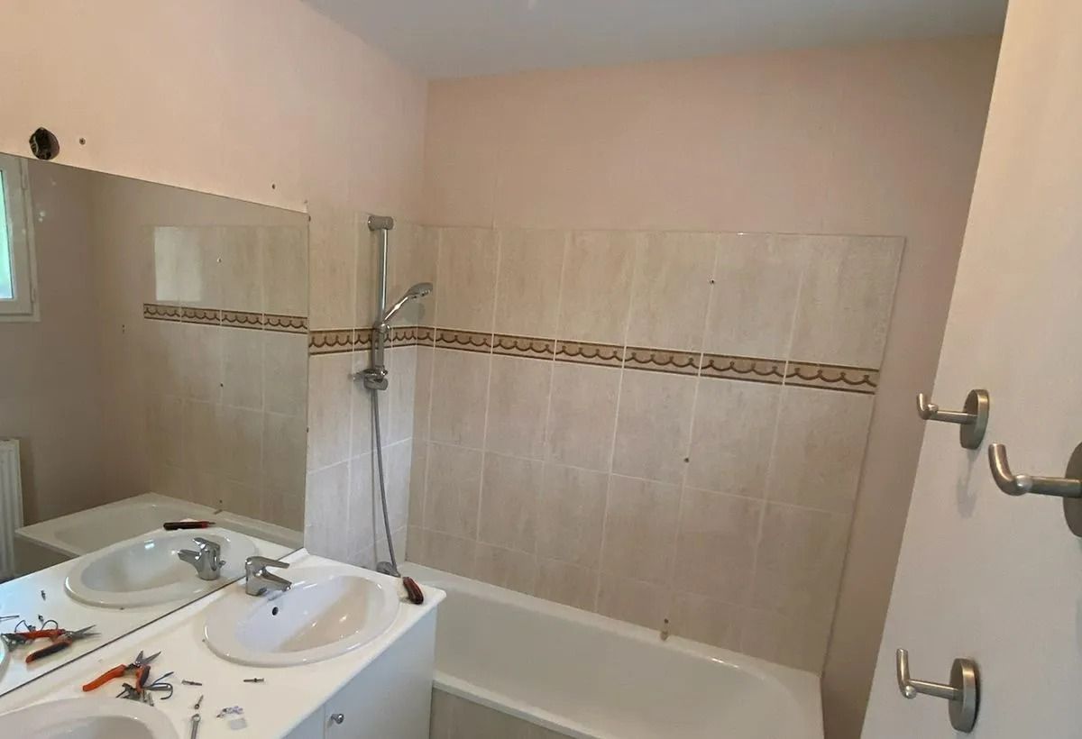 Salle de bains avec baignoire, lavabo, miroir et murs carrelés beiges.