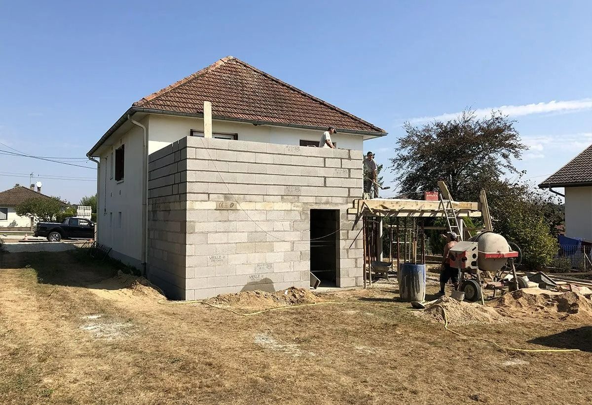 Maison en béton partiellement construite avec un toit de tuiles rouges dans une cour rurale sèche