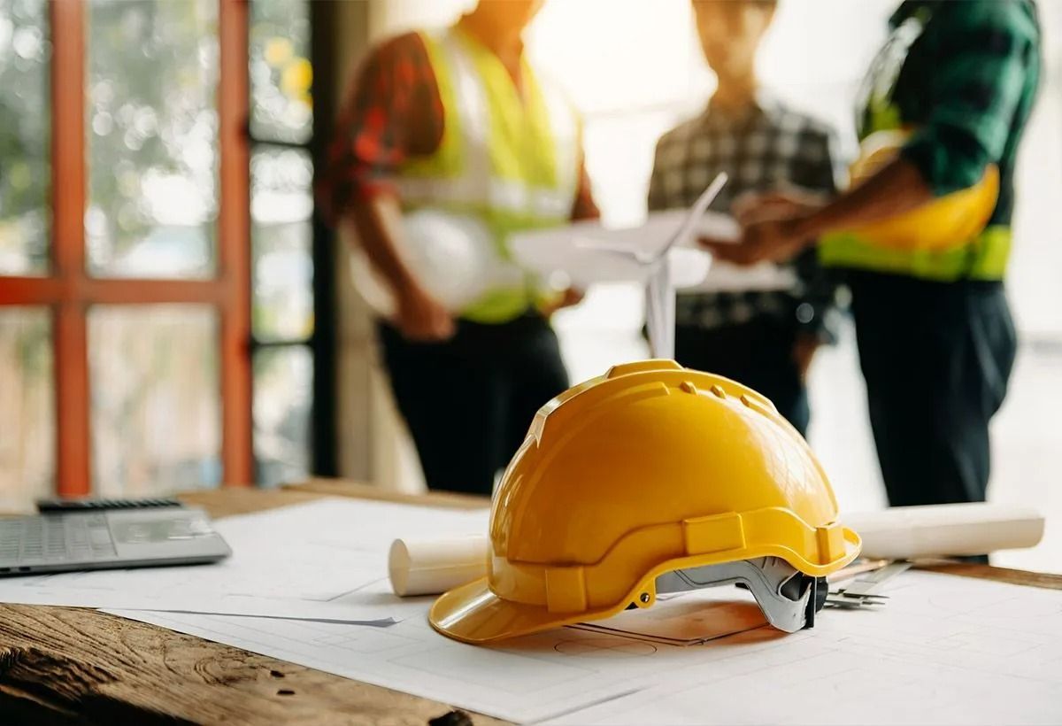 Casque de chantier jaune sur un plan de chantier, avec des ouvriers en gilet réfléchissant en arrière-plan.