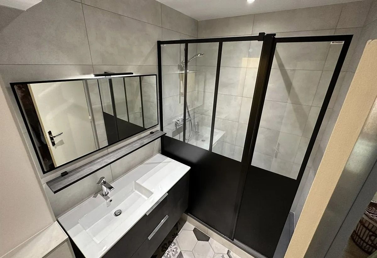 Salle de bains moderne avec lavabo blanc, grand miroir et cabine de douche en verre à cadre noir