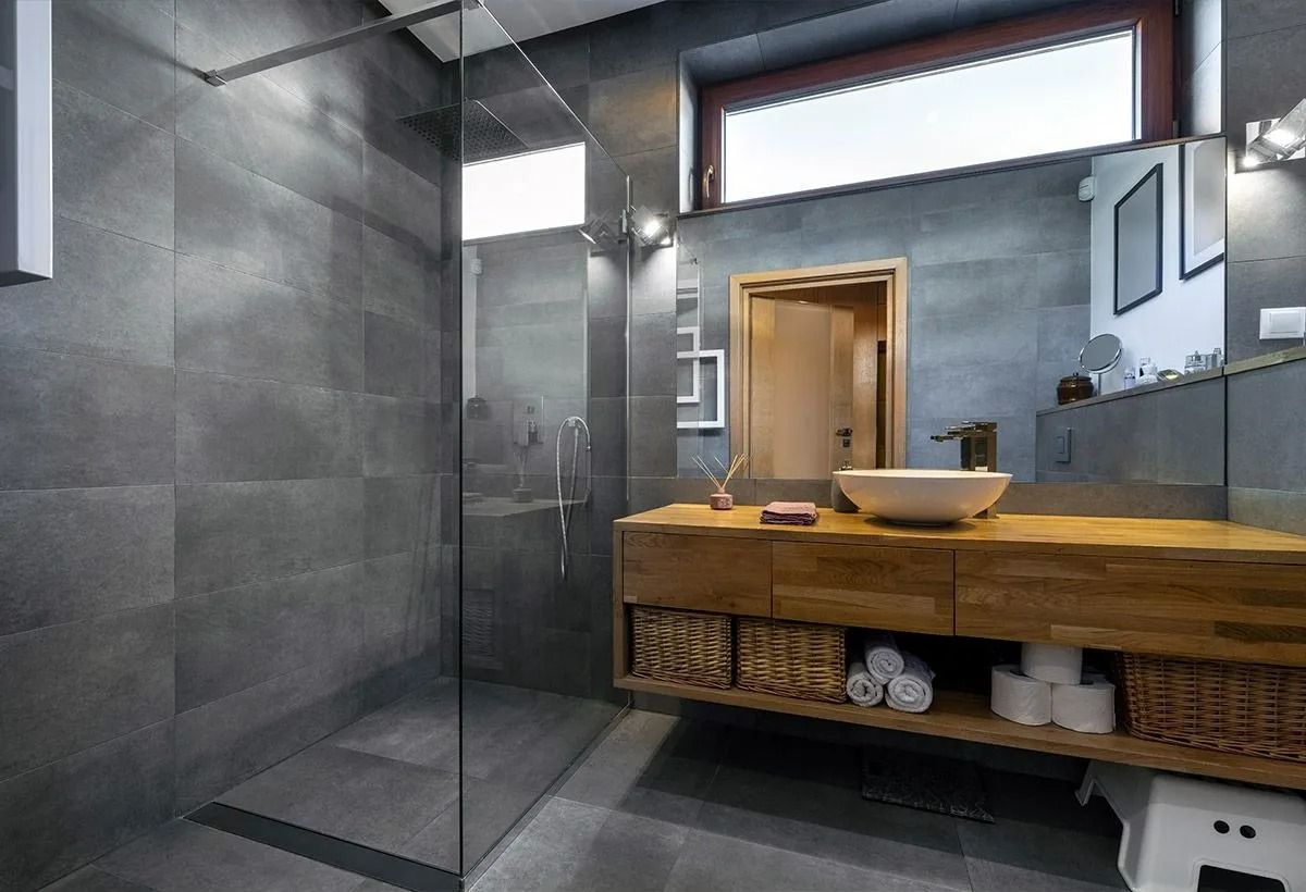 Salle de bains moderne avec murs carrelés gris, meuble-lavabo en bois, miroir et cabine de douche.
