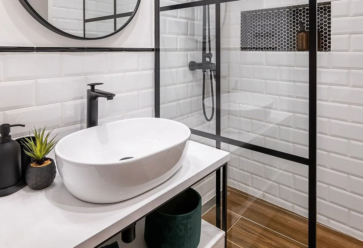 Salle de bains moderne avec lavabo blanc, robinetterie noire et cabine de douche en verre
