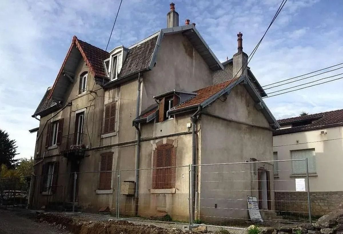 Vieille maison délabrée aux murs fissurés et aux fenêtres condamnées sous un ciel nuageux