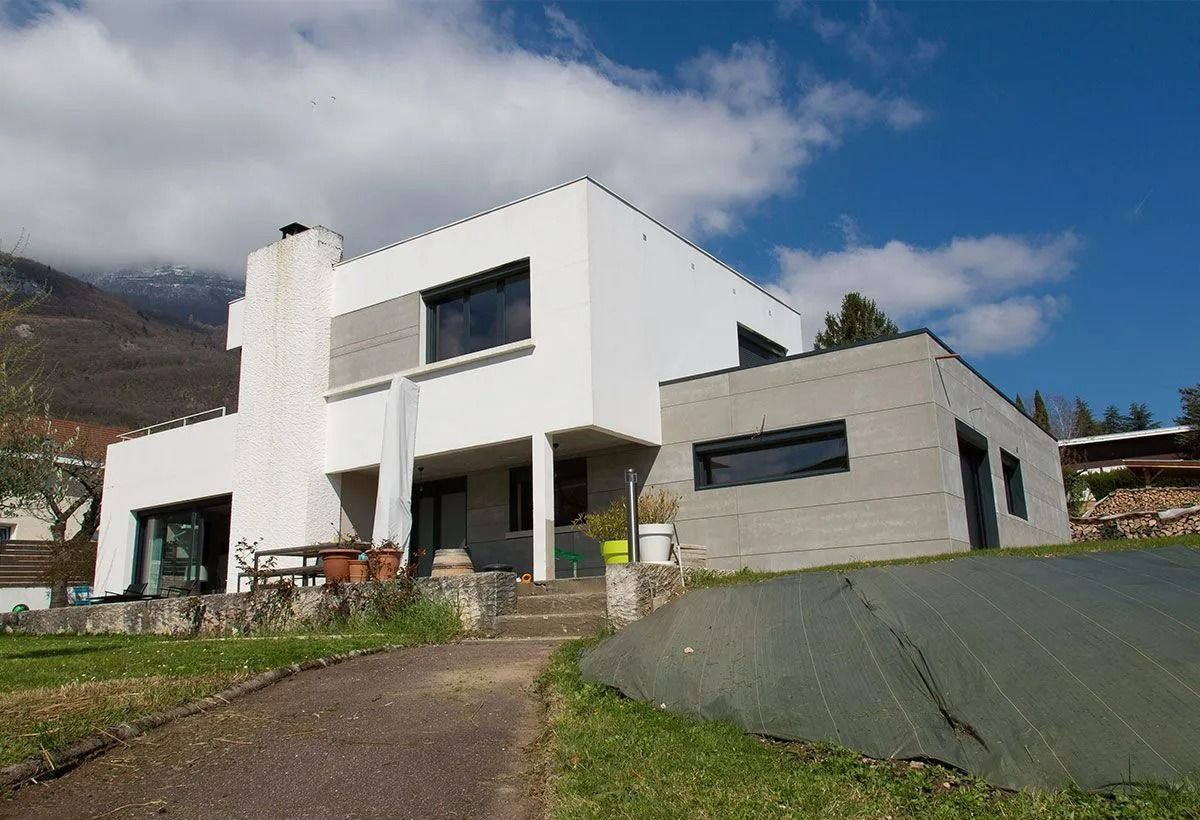 Maison blanche moderne avec des accents de pierre sur une colline sous un ciel bleu