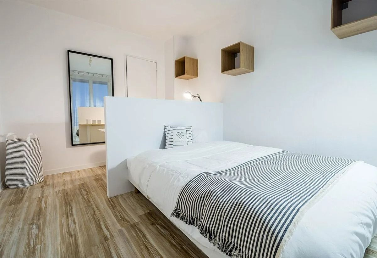 Chambre minimaliste et lumineuse avec un lit blanc, une couverture à rayures, un parquet et des étagères murales