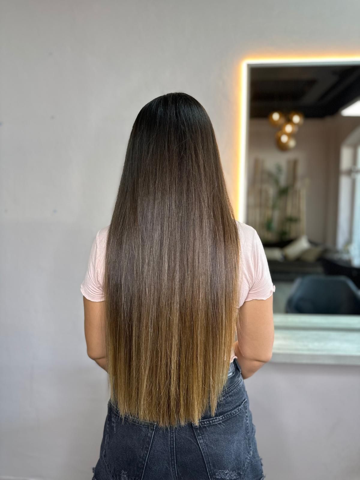 Una mujer con cabello largo está parada frente a un espejo.