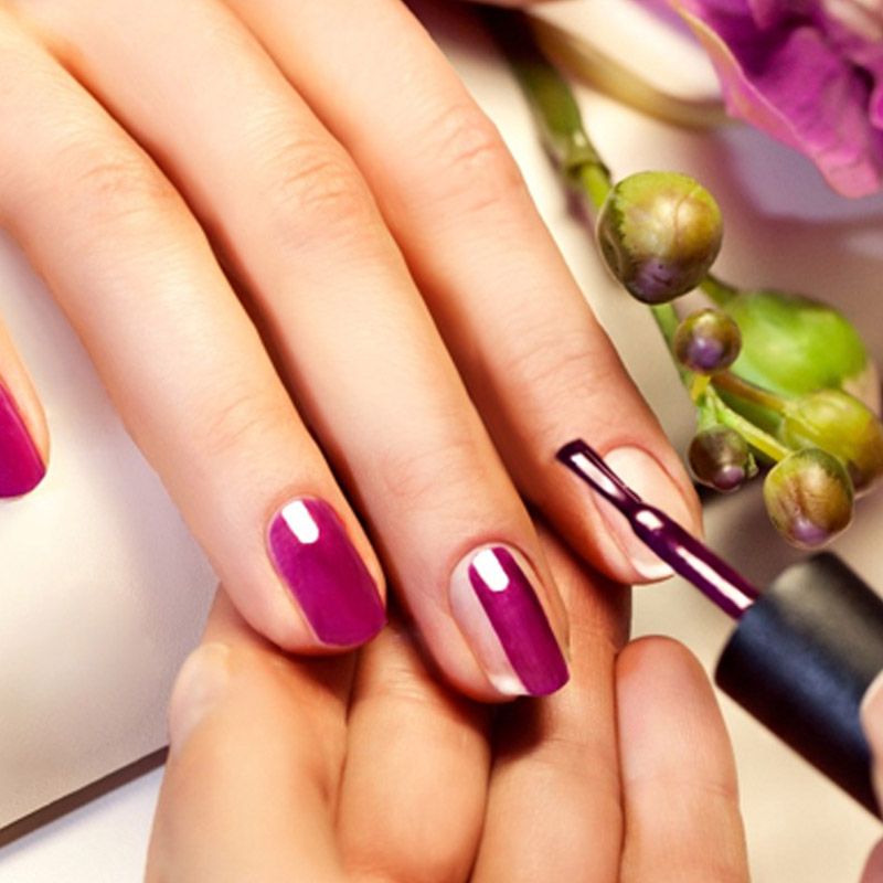 Una mujer se aplica esmalte de uñas morado en las uñas.