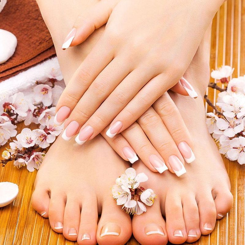 Un primer plano de las manos y los pies de una mujer con flores en el fondo.